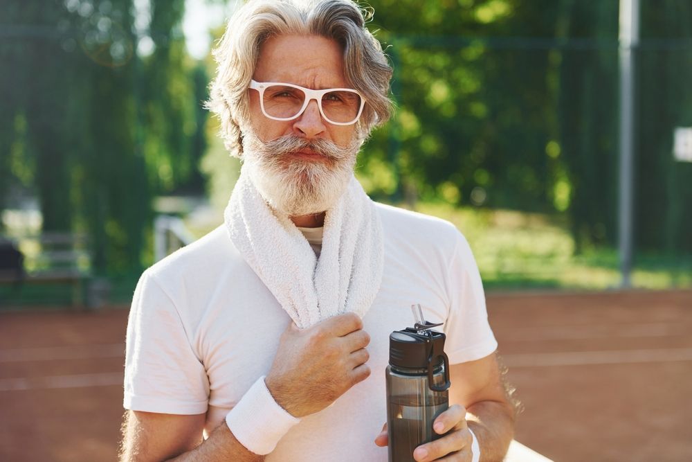 Senior modern stylish man outdoors on the tennis field at daytime wear prescription glasses